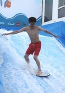 寺山武志/全身・水着赤・サーフィン・両手広げ・目線足元・屋外/「オガステ!?4 ～ タイ マラソン 大阪 オガソン♪ やることいっぱいでどうしよ平八郎の乱 ～」トレーディングブロマイド