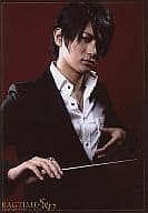 篠谷聖/上半身・スーツ黒・シャツ白・背景茶色・右手指揮棒・左手胸元舞台「RAGTIME S＆D」/公式生写真